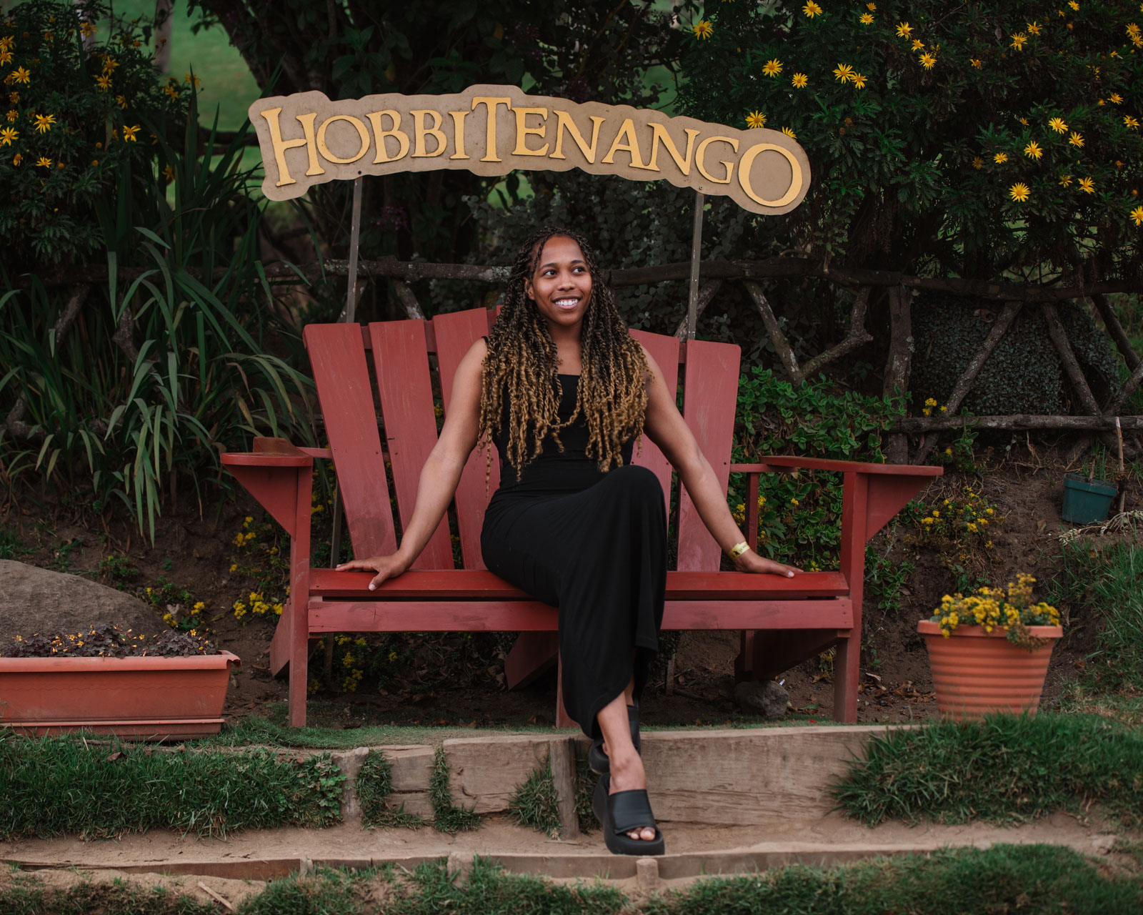 Woman sitting on a giant red chair under a sign that reads, Hobbitenango in Guatemala. Exploring the Best of Guatemala 