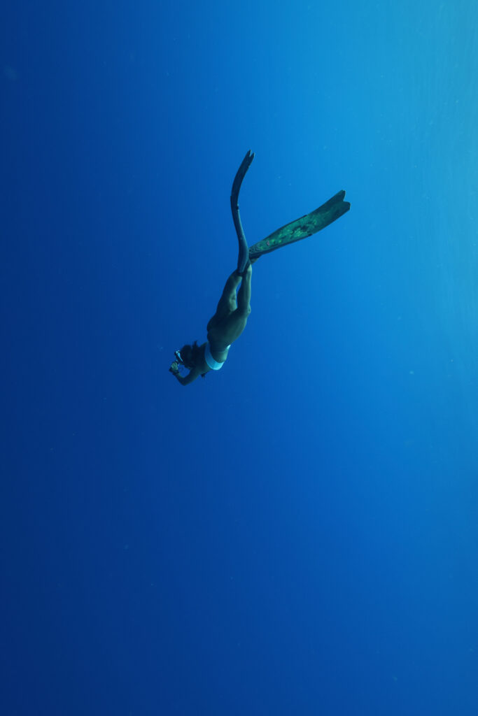 A woman with long fins freediving in the ocean .